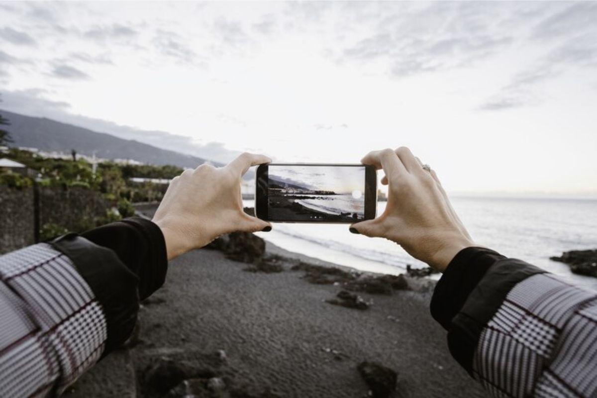 Foto de uma pessoa fotografando o mar com o celular na vertical