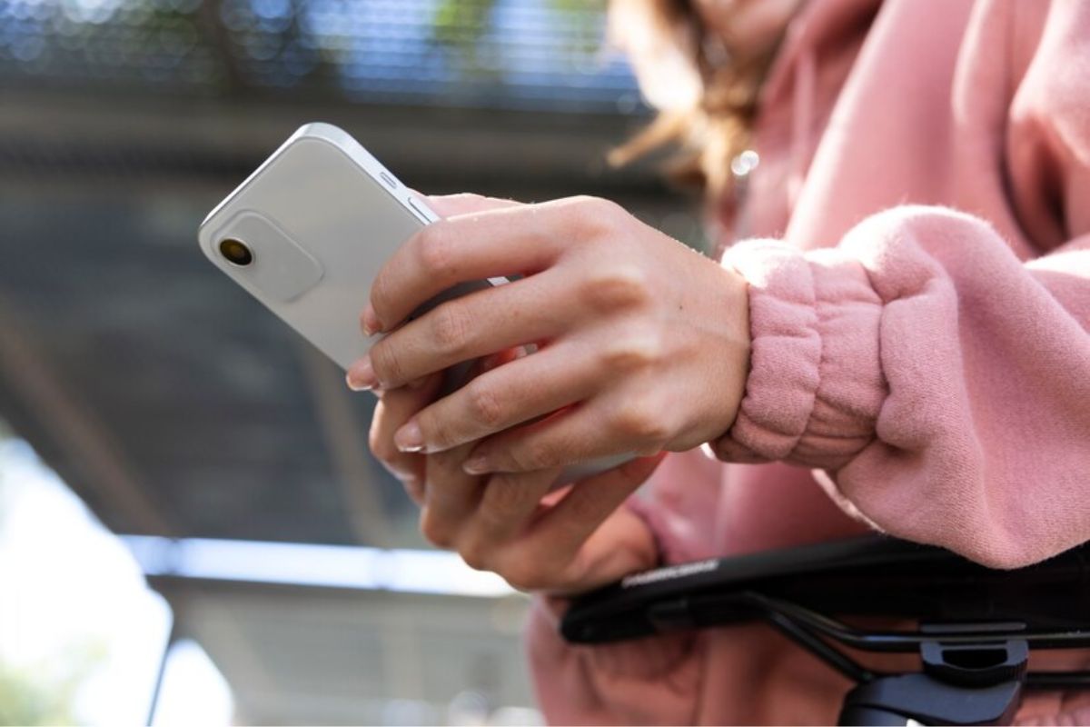 Uma mulher com casaco rosa com o aparelho na mão vê os Melhores Aplicativos para iPhone de 2024