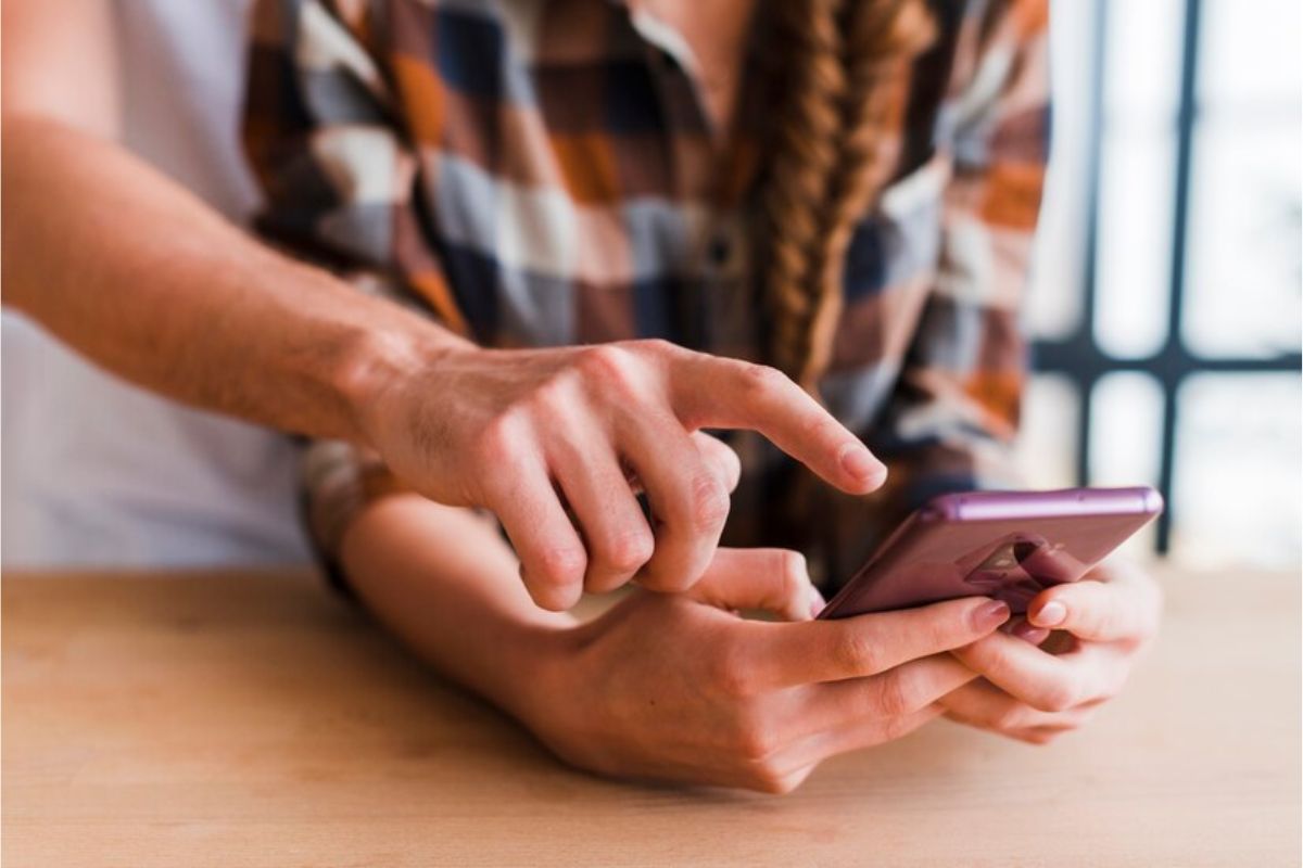 Visão do busto de uma pessoa mexendo no seu smartphone enquanto a outra aponta para algo na tela