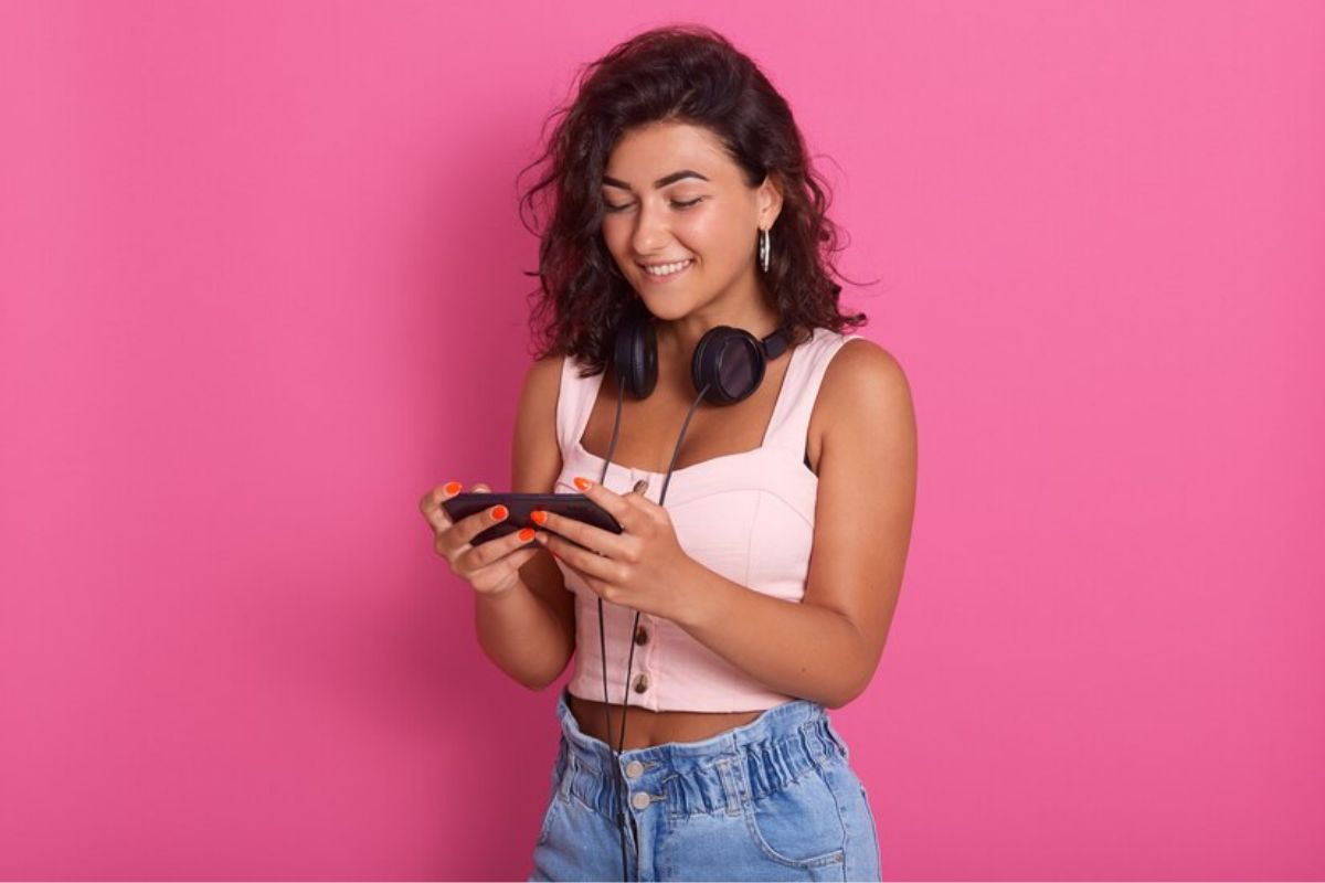 Uma menina na frente de um fundo rosa mexe em seu celular enquanto baixa os Melhores Aplicativos para Motorola em 2024