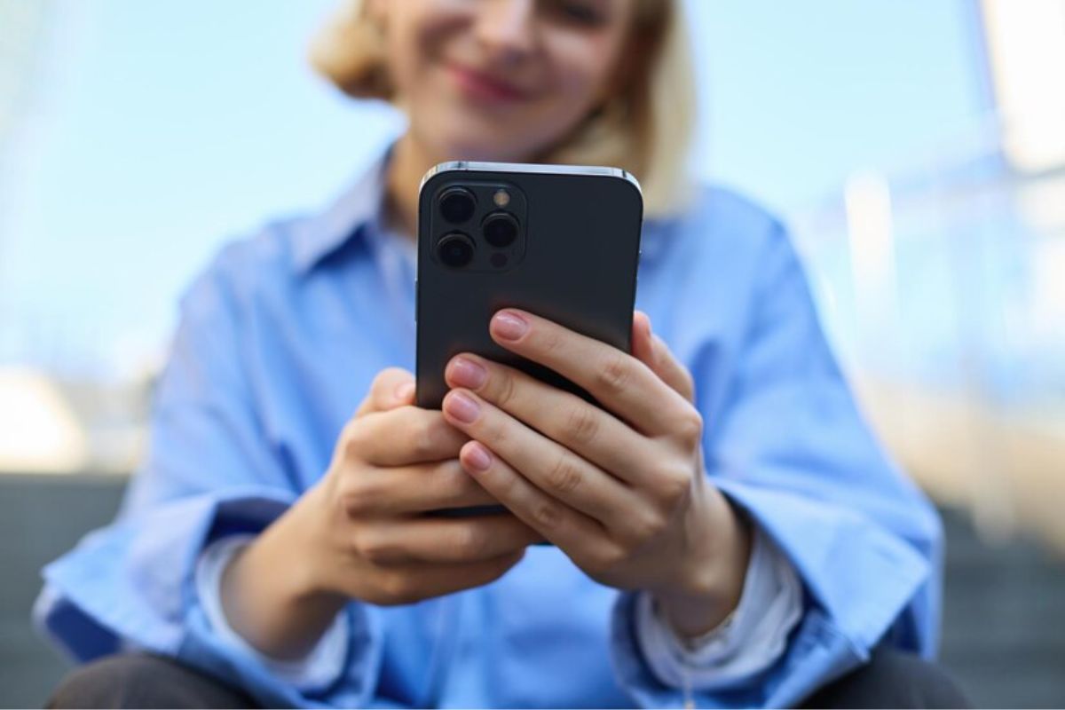 Uma mulher sorri olhando para a tela de seu iPhone que ela segura com as duas mãos