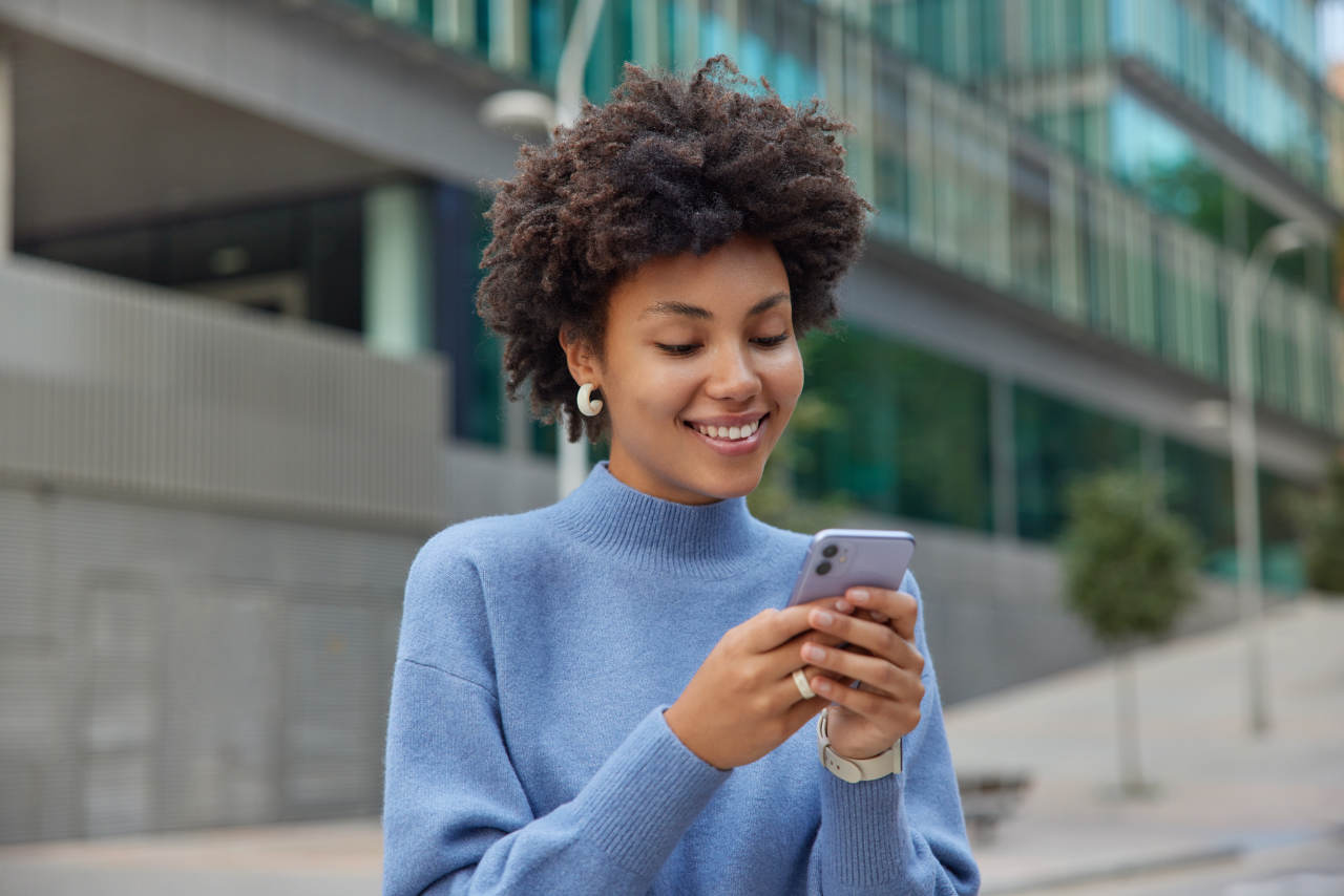 Jovem com cabelo espesso e encaracolado usando um dos melhores celulares da Motorola na rua 