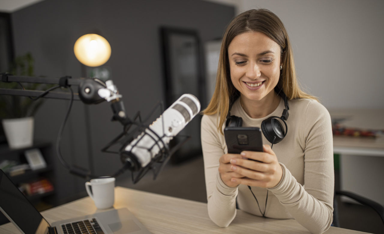 Mulher sorridente fazendo podcast com microfone e smartphone