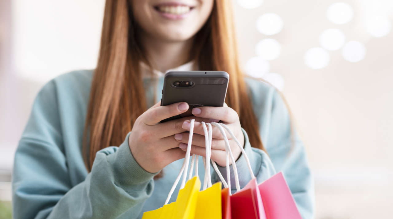 Garota sorrindo com celular e sacolas de compras nas mãos