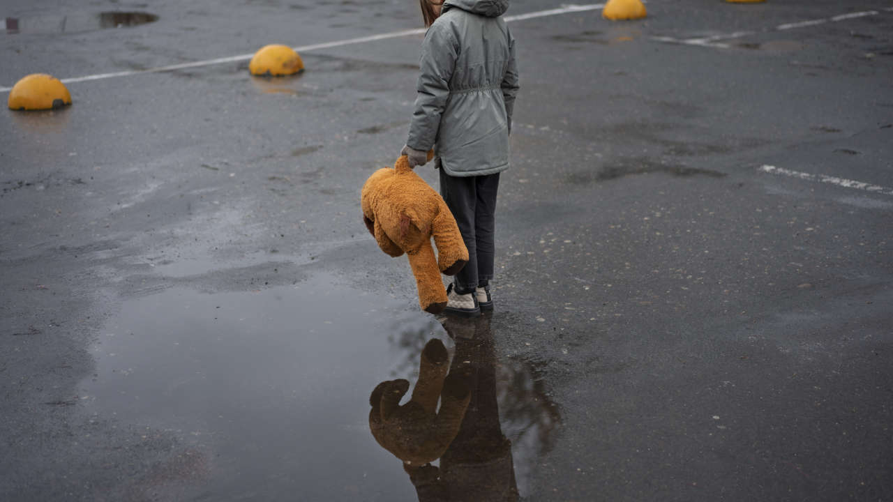 Criança parada com ursinho na mão perto de poça